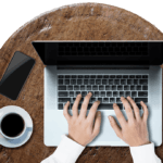 The person is working on his Laptop writing content with a cup of coffee beside him.